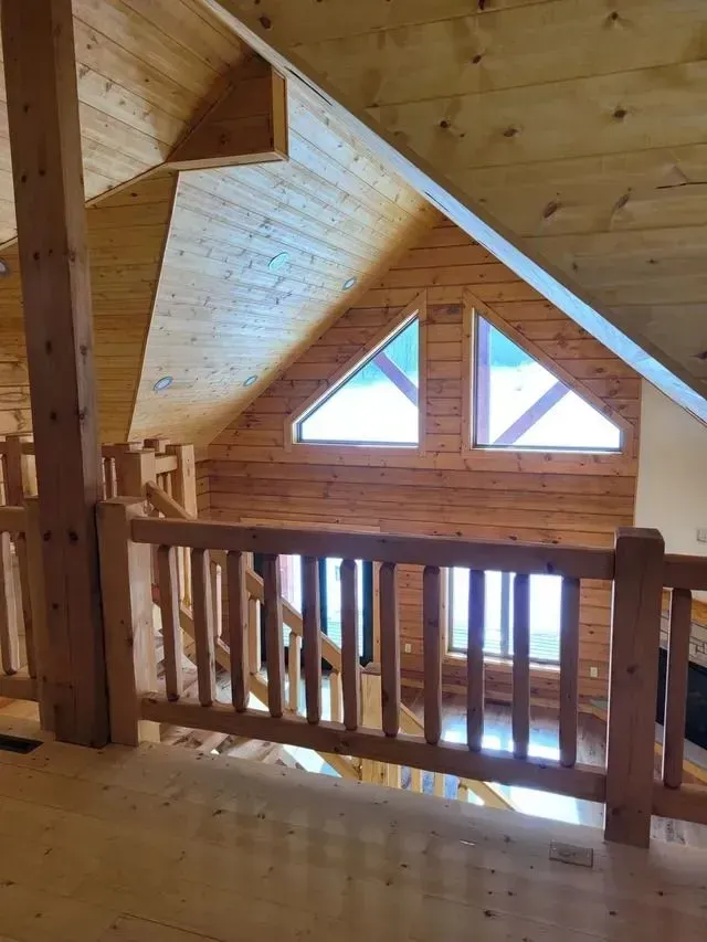 Interior view of a wooden loft with railing and triangular windows in the wall above.
