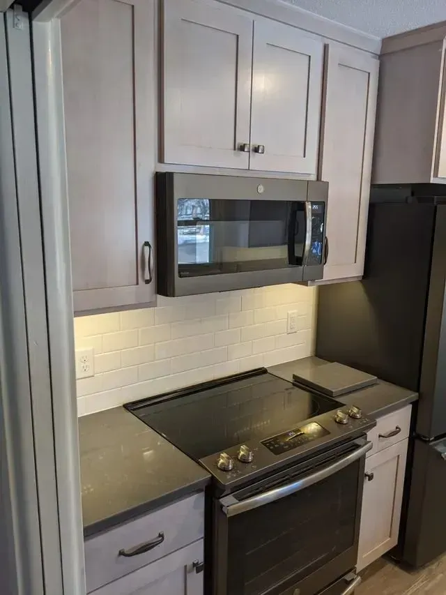 Kitchen with gray cabinets, black appliances, and white backsplash.