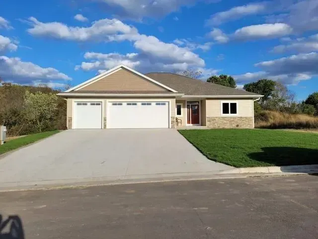 Tan-colored house with a two-car garage, red front door, and green lawn under a blue sky.