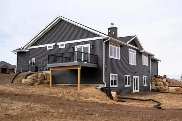 Dark gray house with white trim, a deck, and rock landscaping under a cloudy sky.