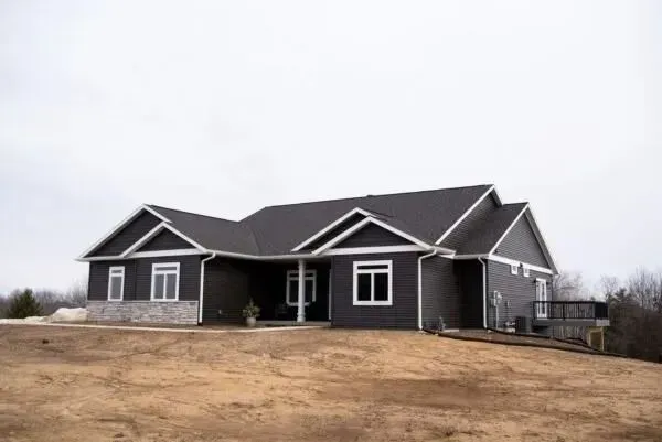 Dark gray house with white trim, stone accent, and deck on brown hillside under overcast sky.