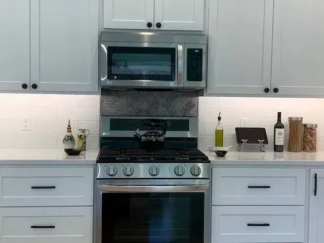 Modern kitchen with white cabinets, stainless steel appliances, and a gas range. Countertop with accessories.