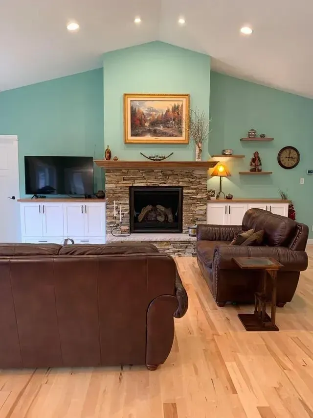 Living room with fireplace, leather sofas, light wood floors, and teal walls.