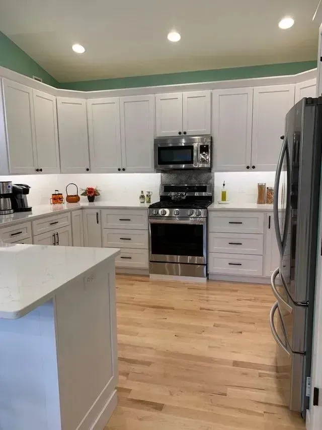 White kitchen with wood floors, white cabinets, stainless steel appliances, and a central island.