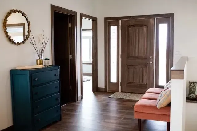 Entryway with teal dresser, oval mirror, and a coral bench. Dark wood door and flooring.