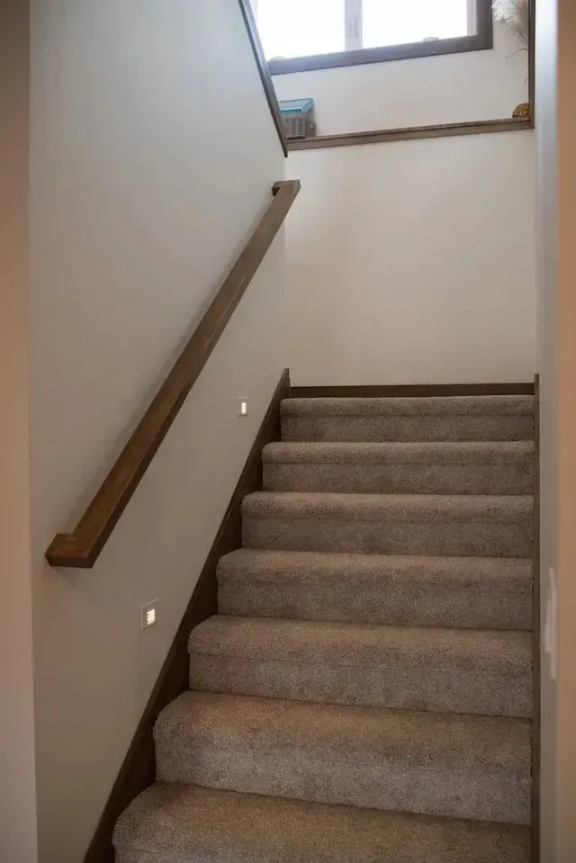 Carpeted staircase with wooden handrail. Wall sconce lighting.