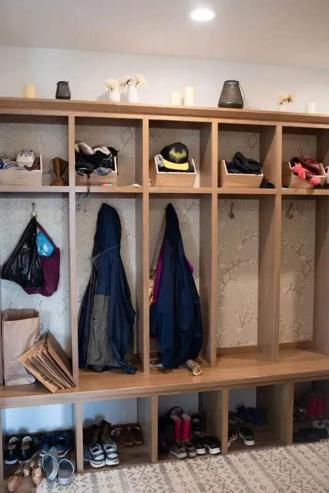 Wooden entryway storage with cubbies, hooks, and bench. Shoes and coats are stored.