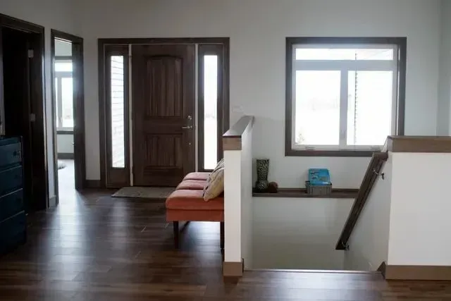 Wooden door, entry area with bench, stairs, and window. Dark wood floors, white walls, and neutral colors.