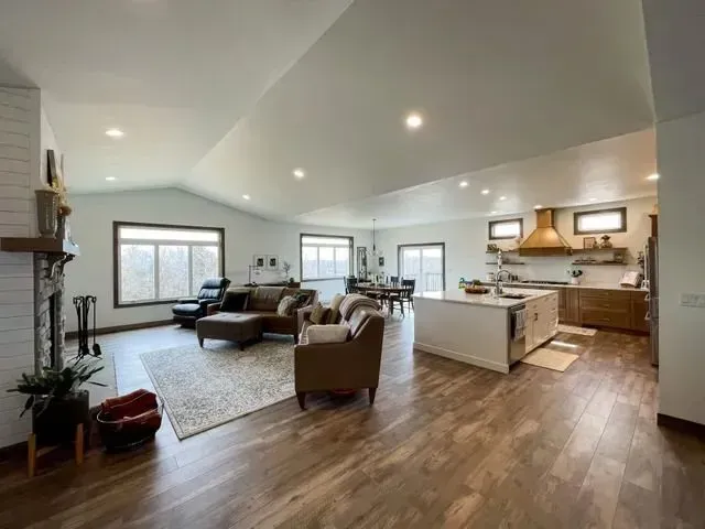 Open-concept living space with a kitchen, living area, and dining room. Hardwood floors, neutral colors, and large windows.