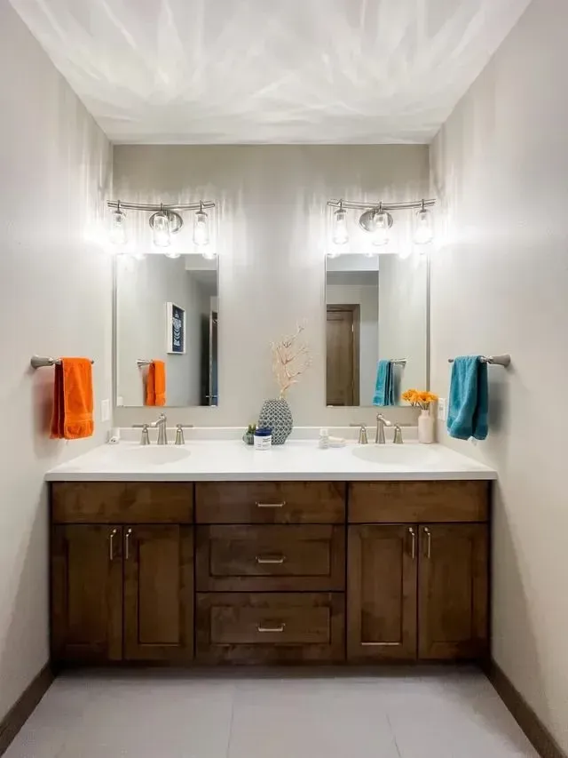 Bathroom with double vanity, two mirrors, and orange and teal towels.