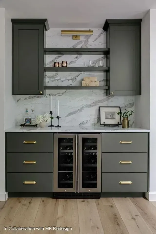 Dark green bar cabinet with marble backsplash, wine fridge, and gold hardware, in a modern home.