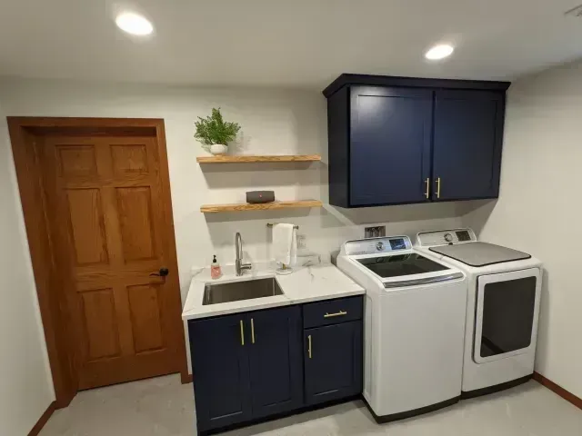 Laundry room with navy cabinets, white appliances, and wood door.