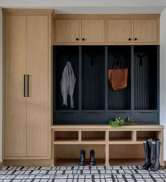 Mudroom with light wood cabinets, black coat cubbies, and shoe storage. A coat and bag hang.
