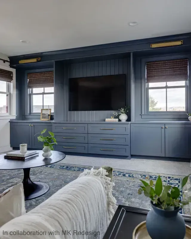 Blue built-in entertainment center with drawers, cabinets, TV, and windows, in a living room with a round coffee table.