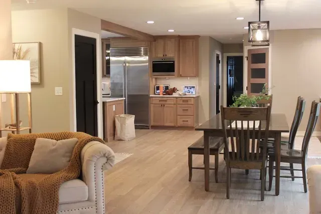 Open-concept kitchen and dining area with wood cabinets, stainless steel appliances, and a dark wood table.