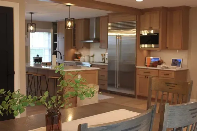 Kitchen with light wood cabinets, stainless steel appliances, and island with bar stools.
