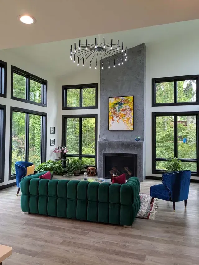 Living room with floor-to-ceiling windows, green sofa, blue armchairs, and a fireplace with artwork.