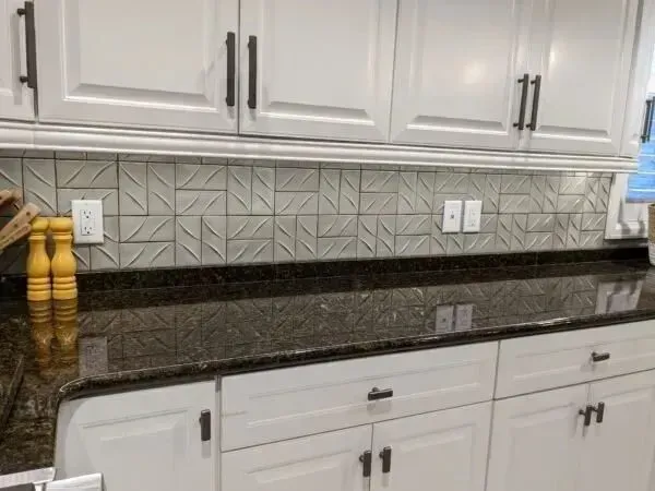 White kitchen cabinets with black hardware, a dark countertop, and textured backsplash.