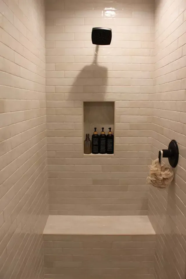 Tiled shower with built-in bench and shampoo niche. Black showerhead, faucet, and toiletries.