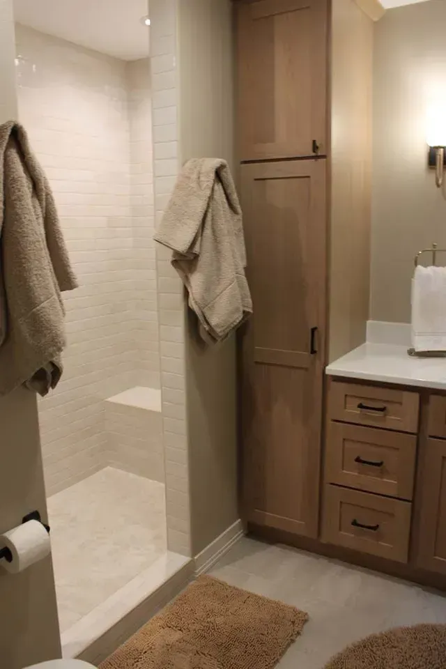 Bathroom with shower, storage cabinet, and vanity. Beige walls and towels, light floor.
