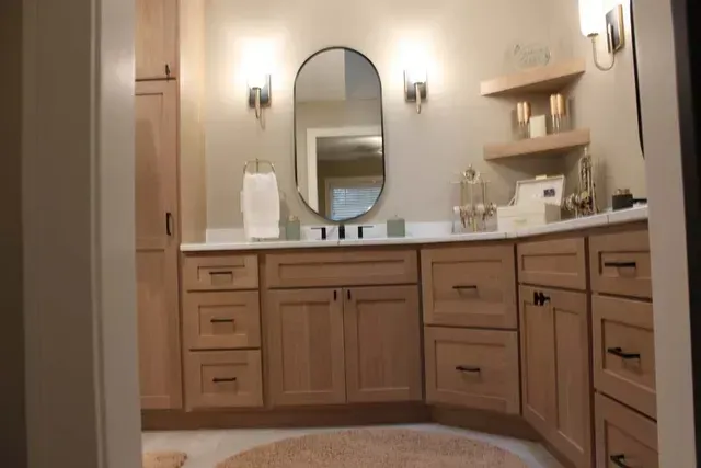 Bathroom with light wood cabinets, oval mirror, white countertop, and beige walls.