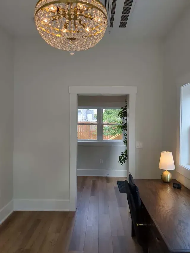 Room with hardwood floors, a desk, doorway to a window, and a crystal chandelier.