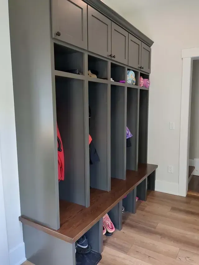Gray storage unit with cubbies, cabinets, and a bench; shoes visible.