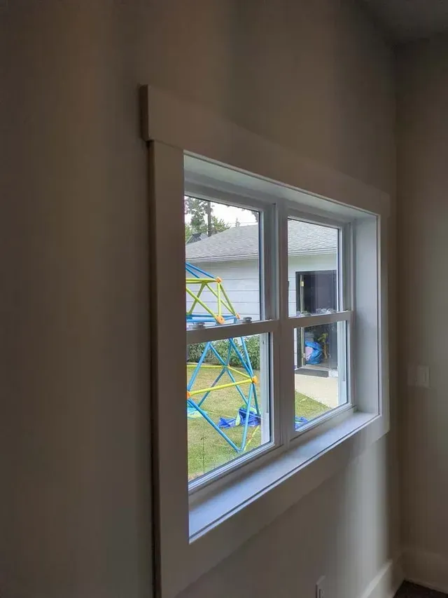 White-framed window with white trim against a light beige wall, looking out at a backyard with a playground.