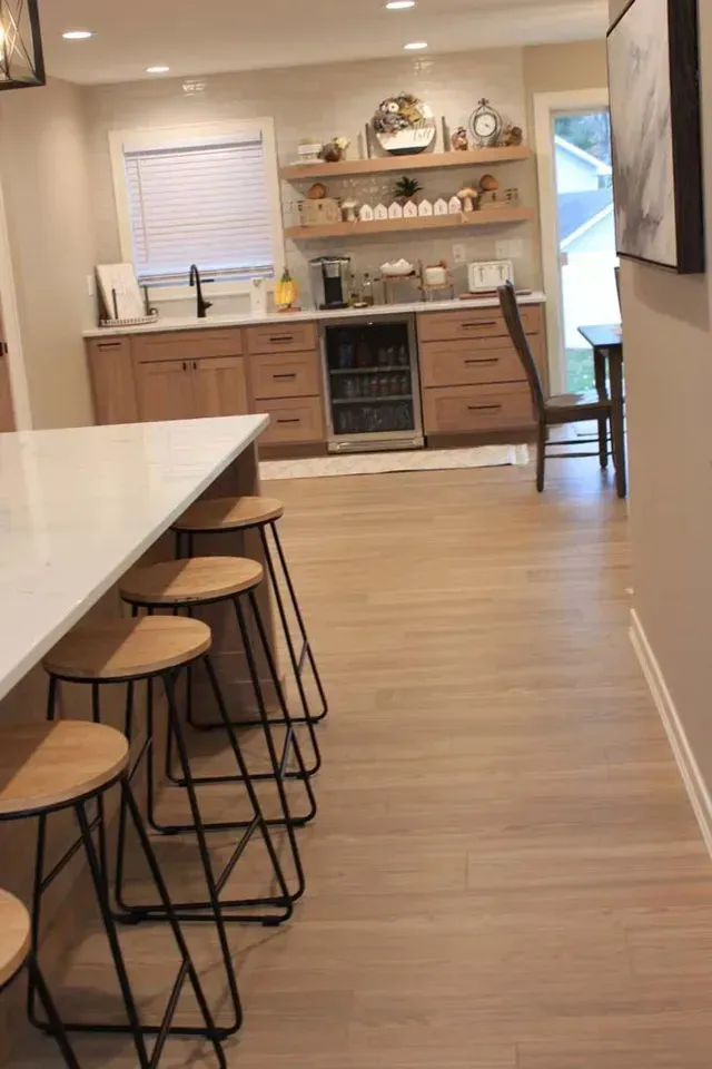Kitchen with island and stools, wood cabinets, floating shelves with decor, and a built-in beverage cooler.