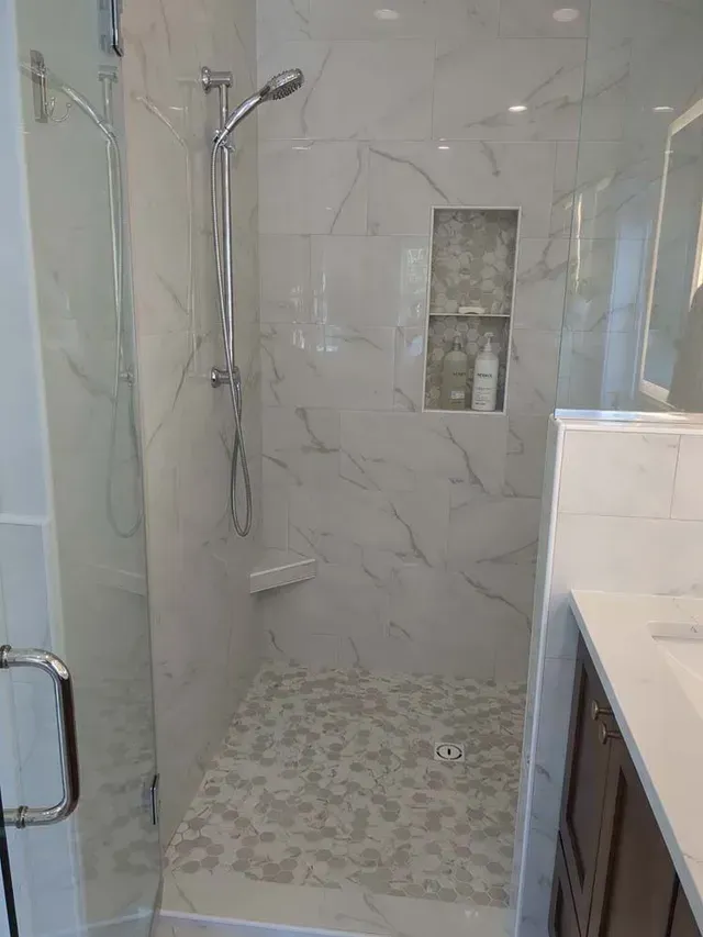 Marble-tiled shower with built-in shelves. Includes a shower head and a pebbled floor.