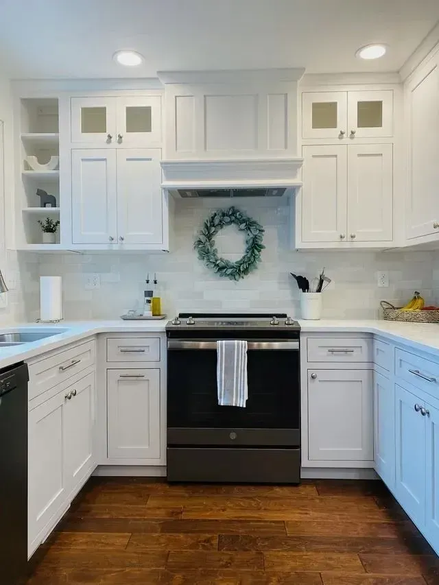 White kitchen with dark wood floors, white cabinets, and a black stove. A wreath hangs above the stove.