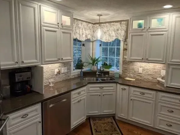 White kitchen cabinets with granite countertops, stainless steel appliances, and a window above the sink.