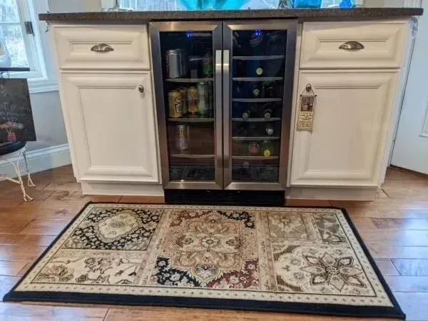 Kitchen island with white cabinets and a built-in beverage center; a patterned rug is on the hardwood floor.