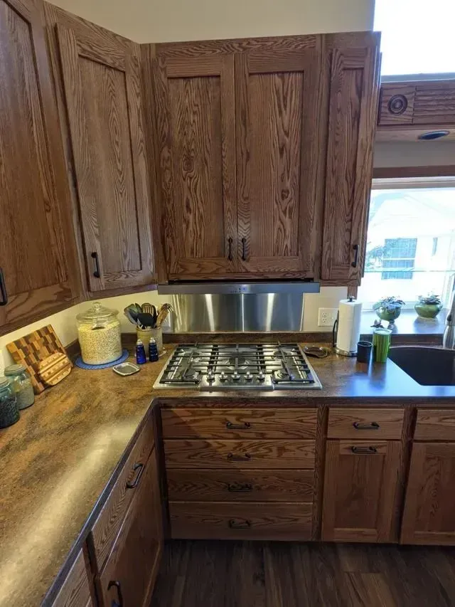 Brown wooden kitchen cabinets with stainless steel range hood and stove.