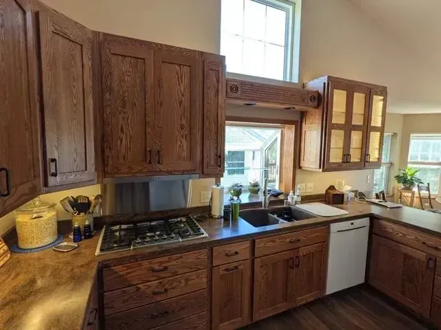 Wooden kitchen with cabinets, stove, sink, and dishwasher. Bright window at the top.