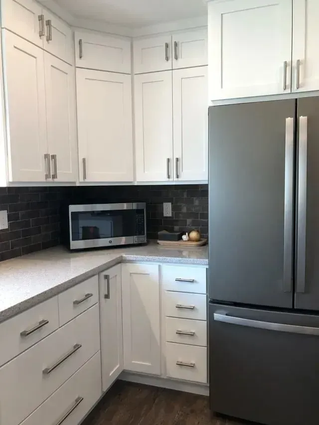 White kitchen with cabinets, stainless steel refrigerator, microwave, and gray countertop.