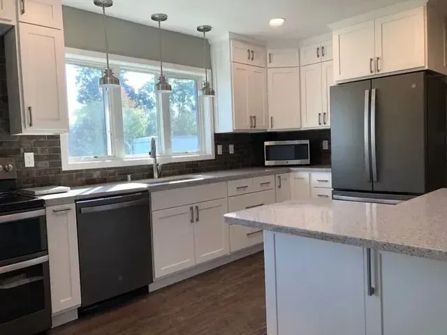Modern white kitchen with stainless steel appliances, granite countertops, and dark cabinets.