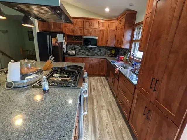 Kitchen with brown cabinets, gray countertops, a stainless steel stove, and a range hood.