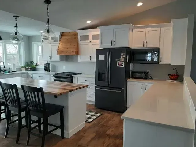 Modern white kitchen with island, black fridge, and wood range hood.
