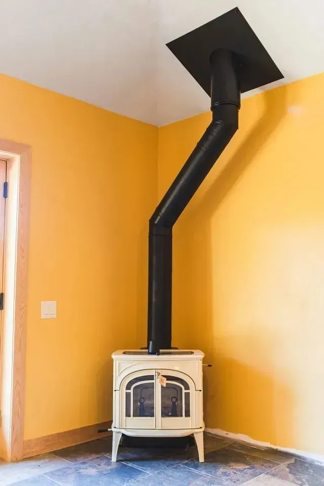 Off-white wood-burning stove with black pipe angled through a yellow-walled corner.