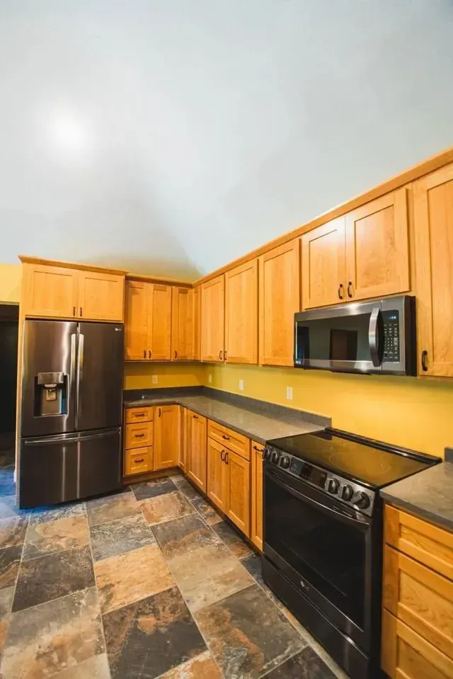 Kitchen with wood cabinets, stainless steel appliances, slate floor, and yellow walls.