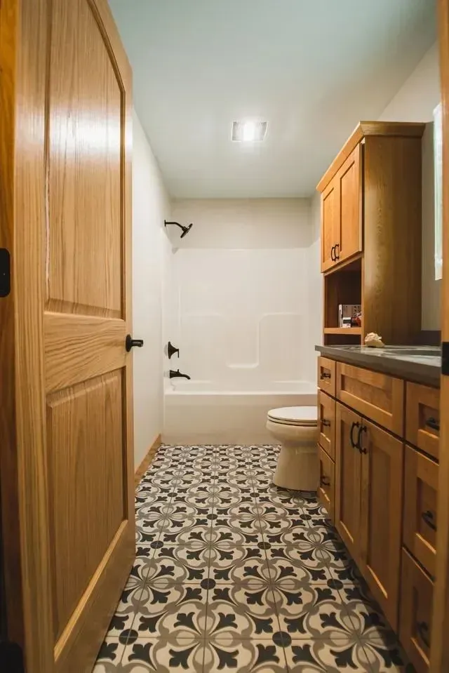 Bathroom with patterned floor, wooden cabinets, tub, and toilet.