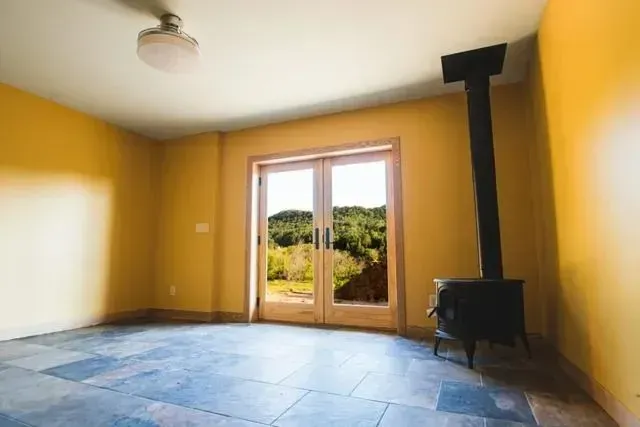 Empty room with yellow walls, slate floor, French doors, wood stove, and outdoor view.
