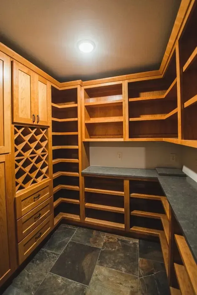Corner pantry with wood shelving, gray countertop, and wine rack. Tile floor.