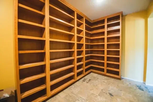 Built-in wooden bookshelves, spanning two walls, in a room with yellow walls and a tiled floor.