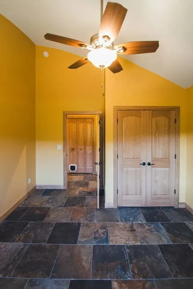 Room with angled yellow walls, slate floor, wooden doors, and a ceiling fan.