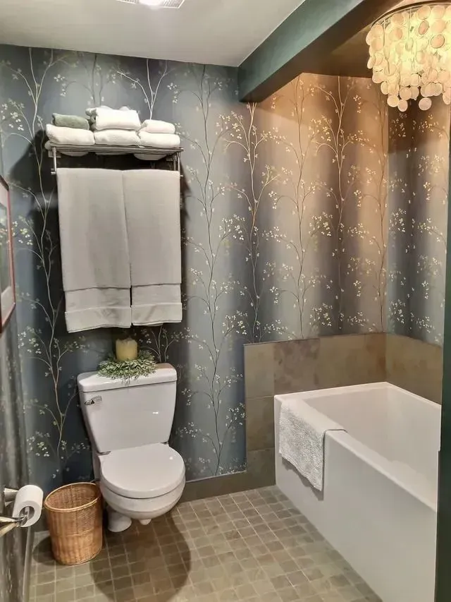 Bathroom with patterned wallpaper, toilet, bathtub, towels, and decorative chandelier.
