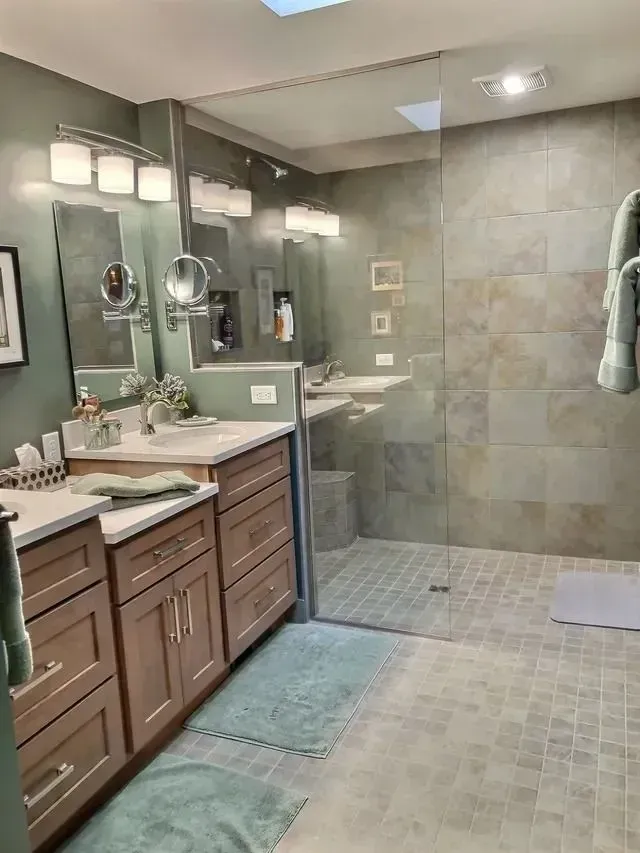 Bathroom with light-colored cabinets, a glass shower, and light green walls and towels.