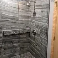 Shower with gray tile, glass door, and silver shower head and handle.