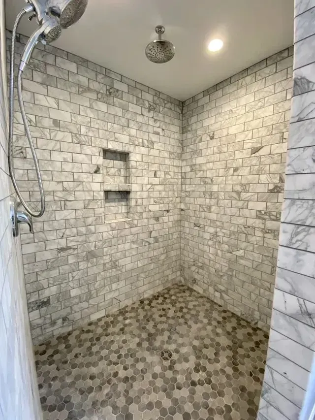 Shower with marble-look brick-like tiled walls, a hexagon tile floor, and built-in shelves.